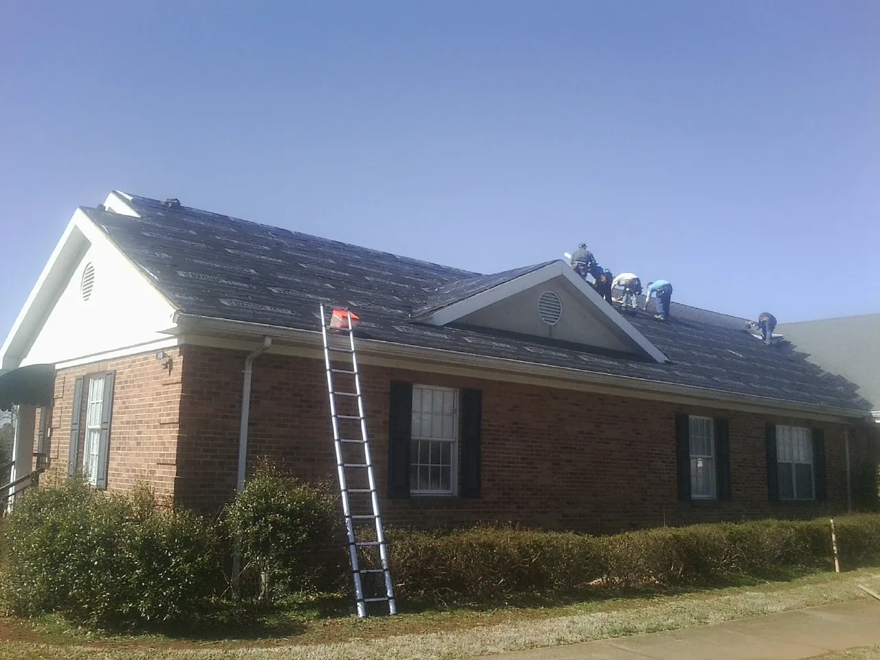 Crew tearing shingles off a brick ranch roof with a ladder set — Emergency Roof Repair work by our crew in Mims