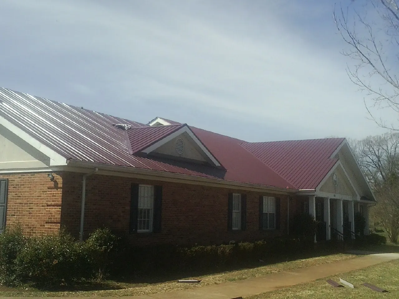 Red metal roof with gabled entries on a long brick building, from a Hail Damage Roof Repair job in Mims