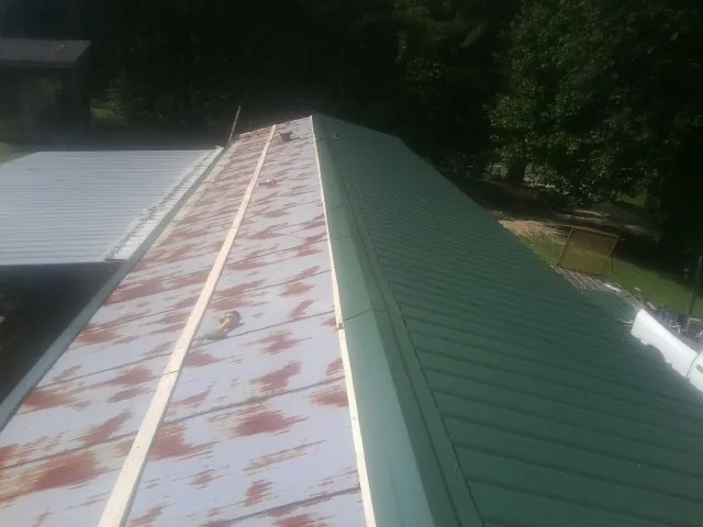 Old rusted panels beside newly installed green metal roofing — Wind Damage Roof Repair by Roofing Brothers in Mims