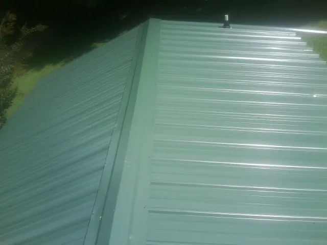 New green metal panels meeting at the ridge of a roof — Flat Roof Repair work by our crew in Mims