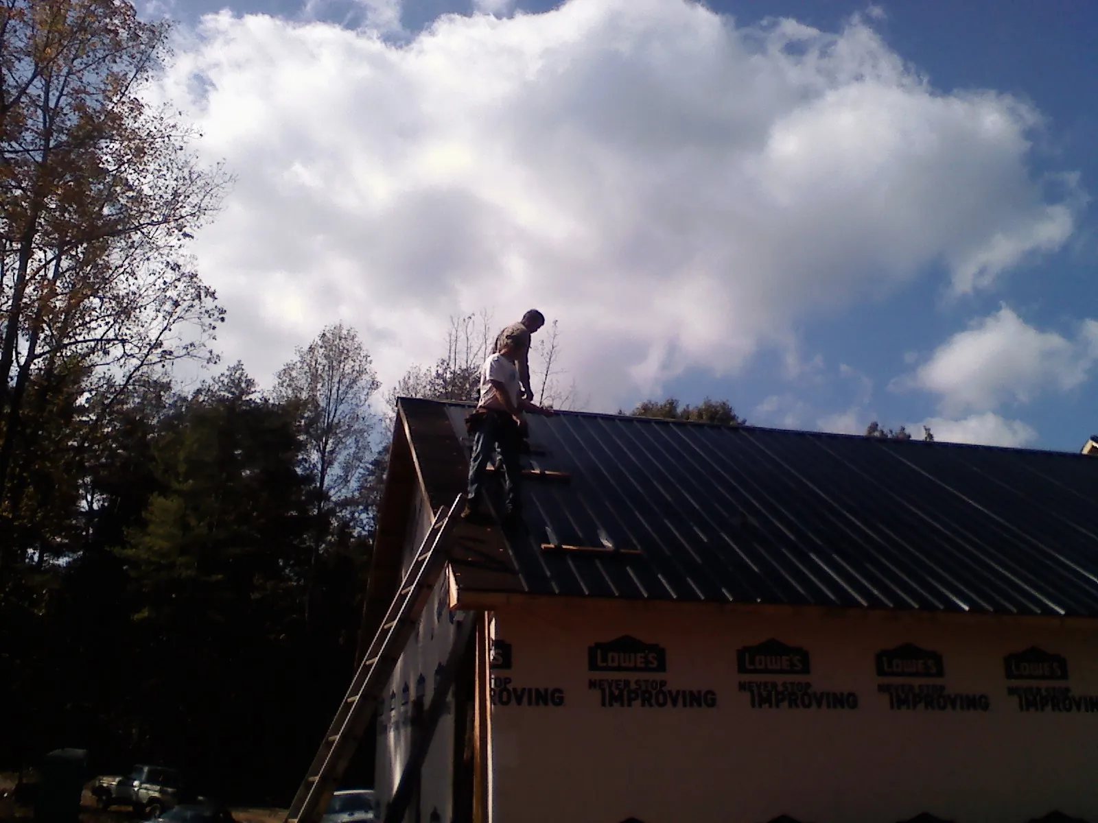 Roofer fastening dark metal panels high against a cloudy sky, from a Roof Inspection job in Mims