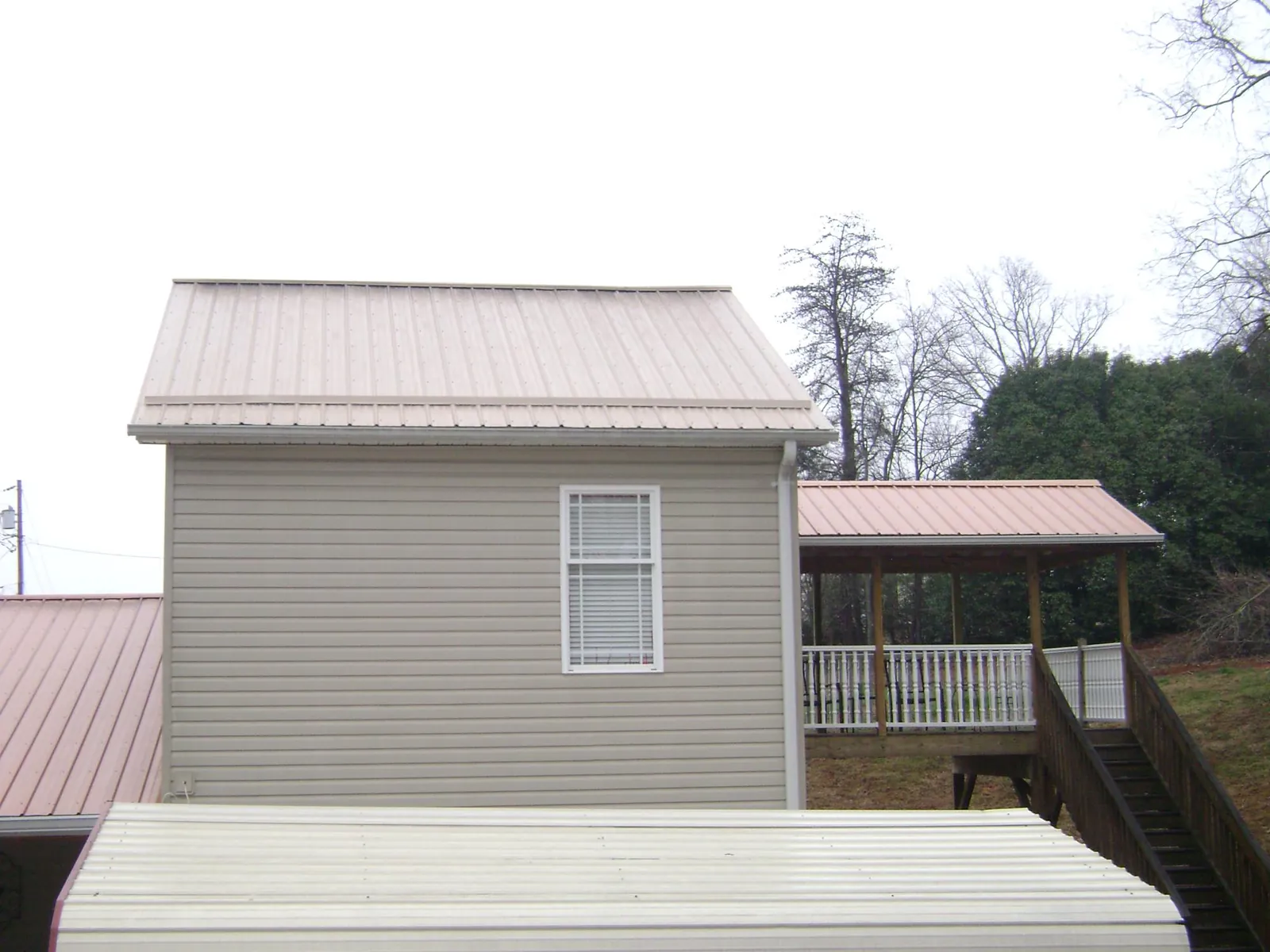 Tan metal roofs on a two story addition and attached porch, from a Roof Replacement job in Mims